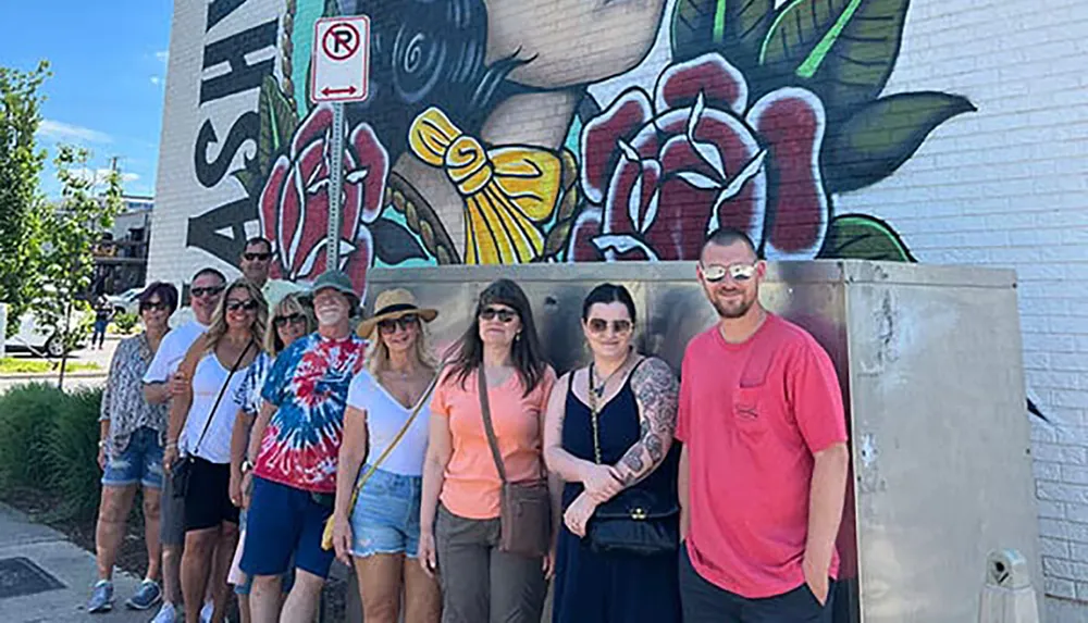 A group of people is posing for a photo in front of a large mural with vibrant artwork on a sunny day