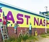 A group of people is posing for a photo in front of a large mural with vibrant artwork on a sunny day