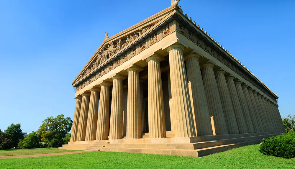 The image showcases a large classical-style building with towering columns and pediments reminiscent of ancient Greek architecture set against a clear blue sky