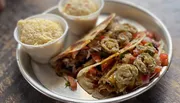 The image showcases a plate with a quesadilla filled with cheese and vegetables, topped with fried jalapeño slices, accompanied by two cups of what appears to be a side dish like rice or mashed potatoes.