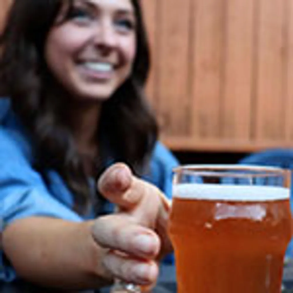 A smiling person reaches for a glass of beer on a table
