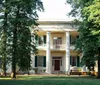 The image shows a stately two-story house with white columns and shutters surrounded by mature trees and a well-kept lawn