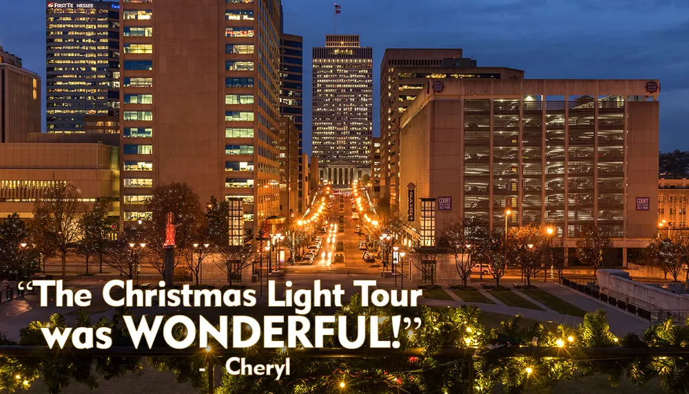 The image captures a dusk view of a city street lined with illuminated buildings decorative lights and a statue all framed by festive garland in the foreground