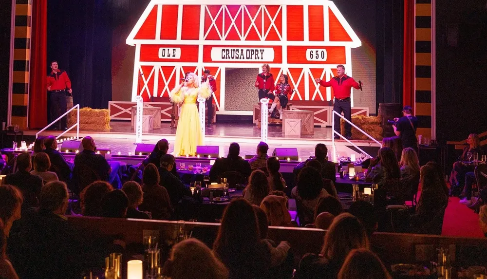 A vibrant stage performance is taking place with a singer in a yellow dress and musicians in red shirts set against a barn-themed backdrop as an audience watches in a dimly lit room