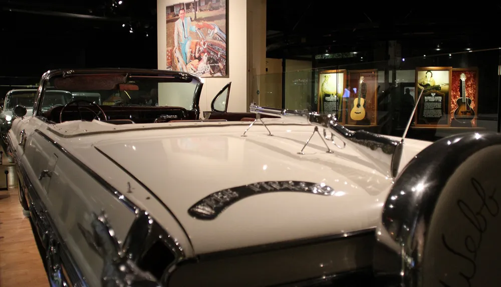 The image shows a classic convertible car on display in a museum with musical instruments and memorabilia visible in the background