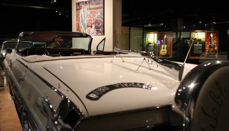 The image shows a classic convertible car on display in a museum with musical instruments and memorabilia visible in the background.