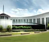 The image shows the Country Music Hall of Fame and Museum with its modern architectural design and distinctive windows located in a large open space with grass and trees under a partly cloudy sky