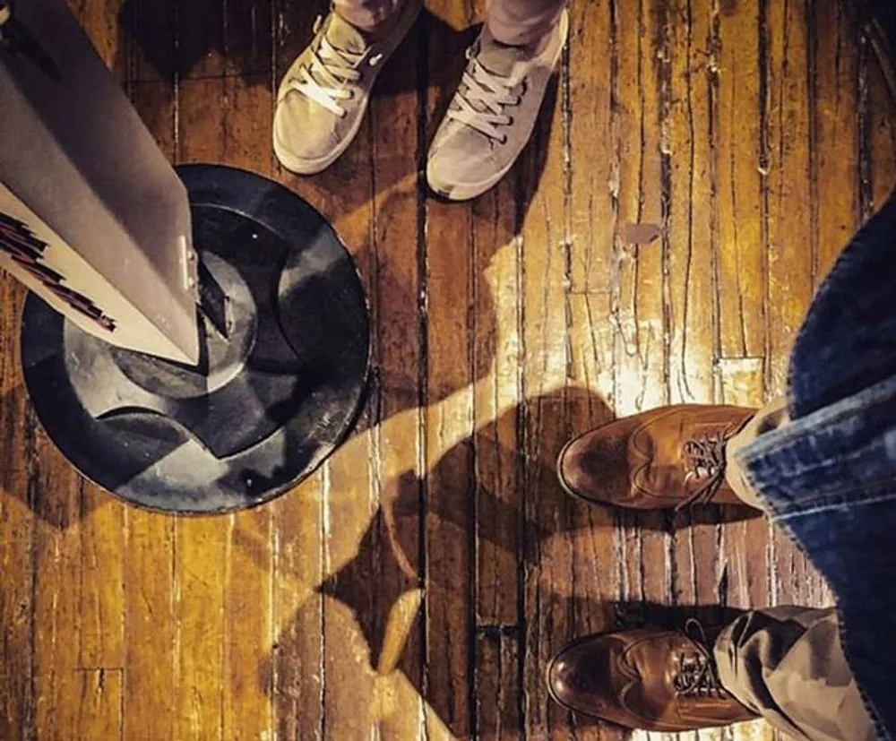 Two people are standing on a wooden floor with one of them throwing away papers in a black spiral-design bin