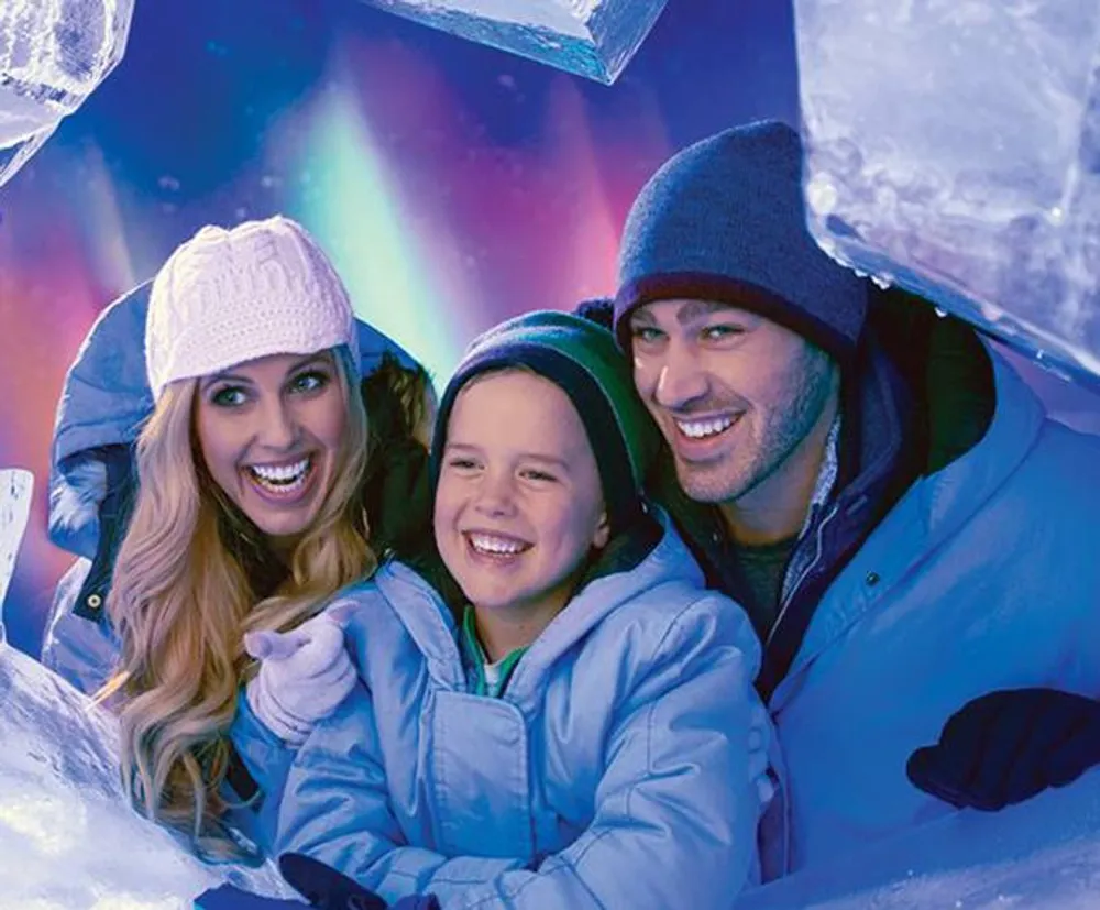 A family is smiling joyfully while peeking through a glistening ice cave under the colorful display of Northern Lights