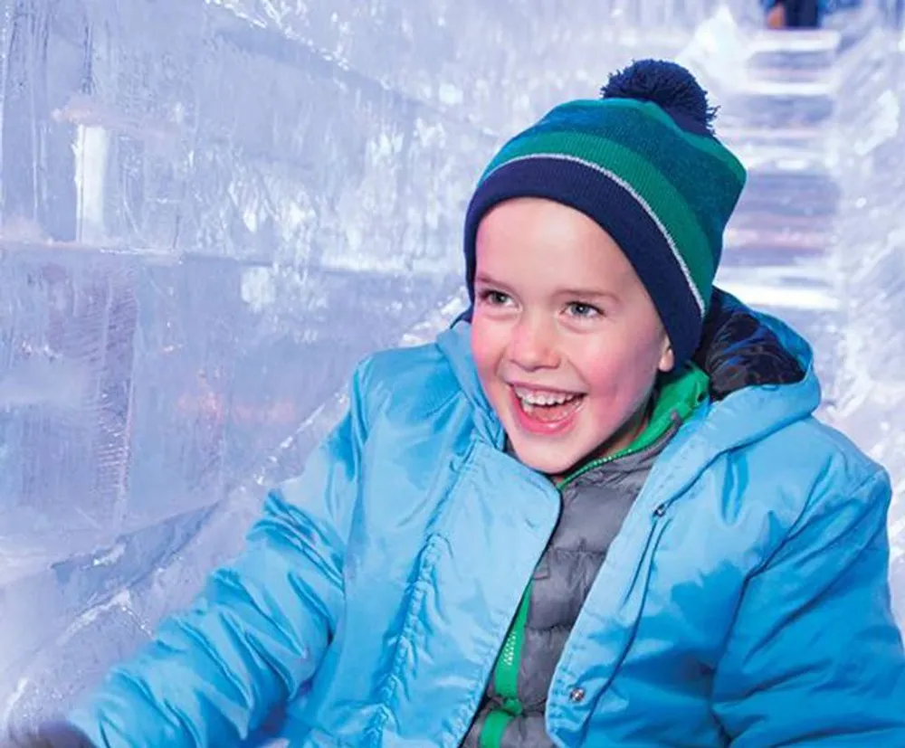 A joyful child in winter clothing is smiling near a wall made of ice blocks