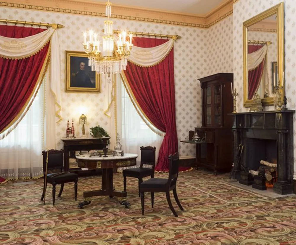 The image shows a classically decorated room with elegant red draperies antique furniture and a chandelier evoking a sense of historical sophistication