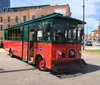 A red and green trolley-like tourist bus is parked on a sunny street with buildings in the background