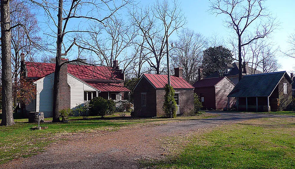 The image shows multiple structures with red roofs possibly historic buildings surrounded by bare trees and a gravel driveway under a clear blue sky