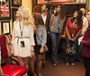 A group of people seemingly on a guided tour are attentively looking at framed posters and memorabilia on the walls of a room decorated with an American flag and various furnishings