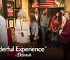 A group of people seemingly on a guided tour are attentively looking at framed posters and memorabilia on the walls of a room decorated with an American flag and various furnishings