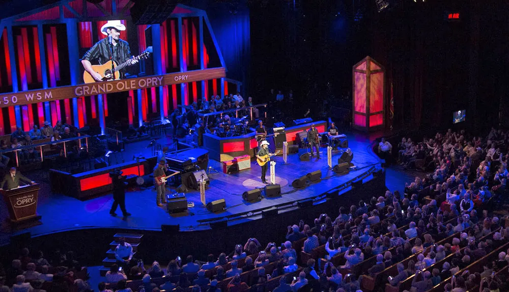A musician donning a cowboy hat performs on stage at the Grand Ole Opry while the audience enjoys the live country music show