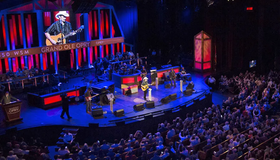 A musician donning a cowboy hat performs on stage at the Grand Ole Opry while the audience enjoys the live country music show.