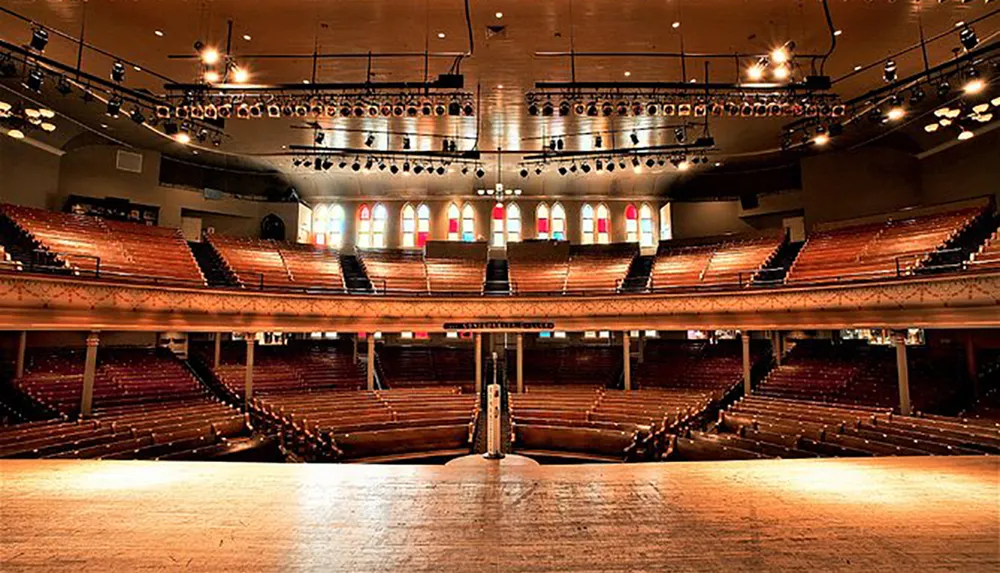 The image shows an empty grand theater with multiple tiers of seating a large stage in the foreground and stage lights overhead