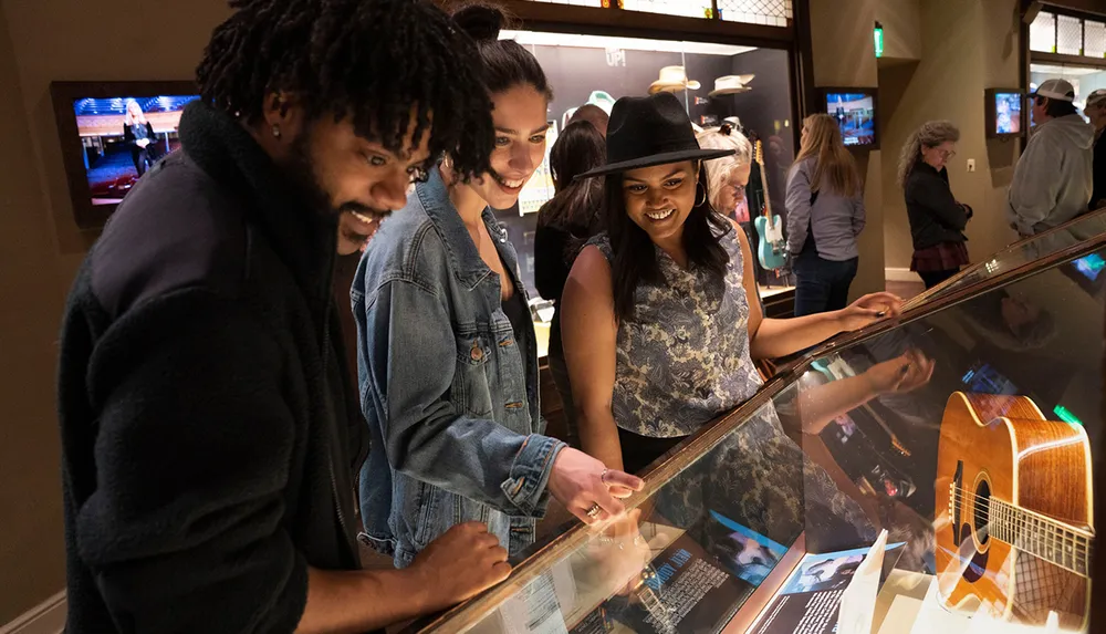 A group of people is smiling and looking at exhibits possibly within a museum or gallery where a guitar is displayed under glass