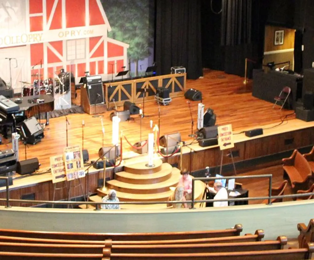 This is an image of the iconic Grand Ole Opry stage set up for a performance with musical instruments and equipment arranged and a few audience members in the foreground