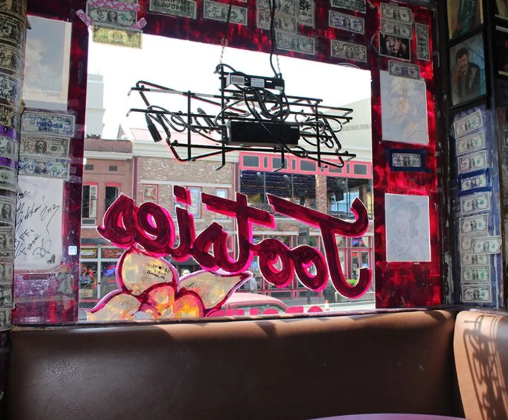 The image shows the interior of a diner with a neon sign in a window that is surrounded by dollar bills and photographs all creating a distinctly Americana vibe