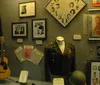 The image shows a display case with various music memorabilia including a decorative guitar photographs clothing a cowboy hat and hand-written notes suggesting a tribute to a musicians career