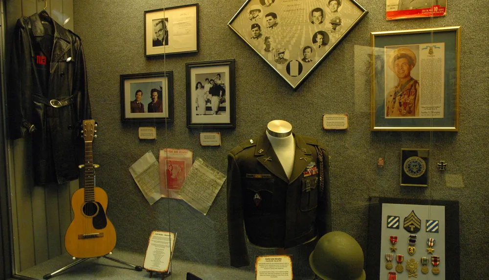 This image depicts a display case filled with military memorabilia including a uniform medals images and personal items likely part of a museum exhibit honoring a soldiers service