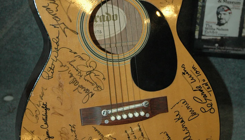 The image shows a close-up of an acoustic guitar adorned with numerous signatures