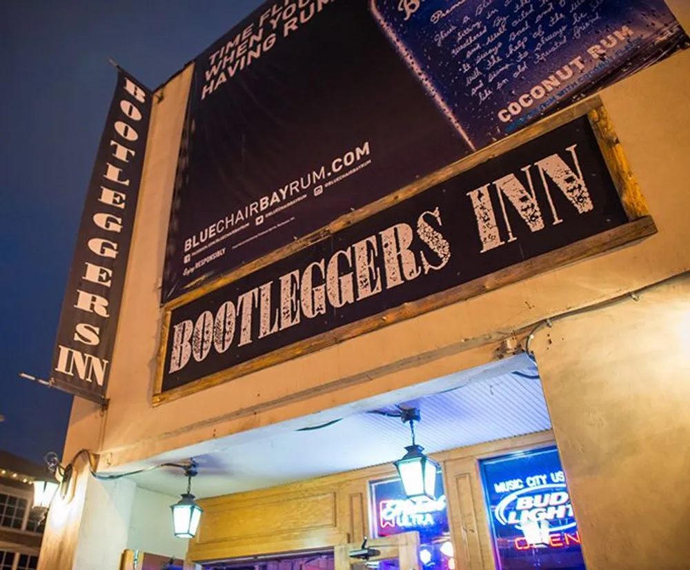 The image shows the exterior of Bootleggers Inn at night with illuminated signs and blue neon lights advertising live music and beer