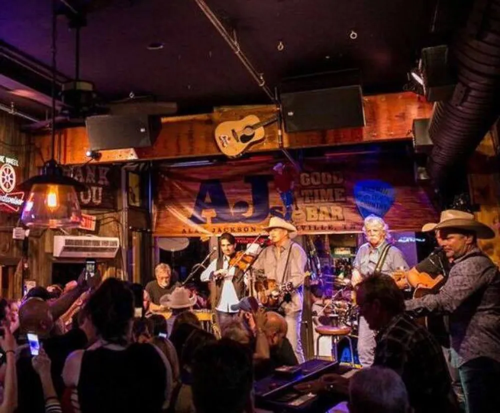 A band is performing on stage at a lively bar while the audience watches and records the event with their phones