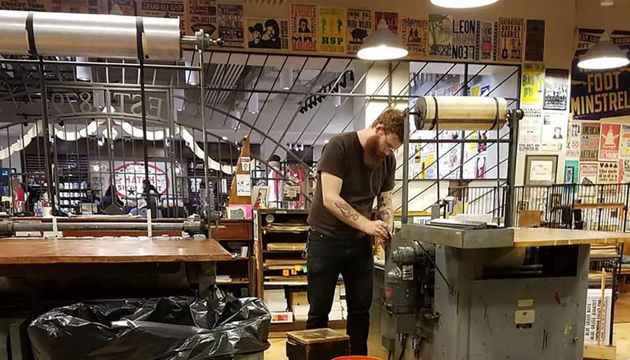 A person is operating a piece of machinery in a workshop-like space adorned with various posters and signs on the walls.