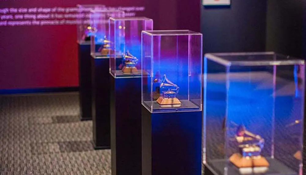 The image shows a series of clear acrylic display cases each mounted on a pedestal showcasing miniature objects under blue lighting in a museum or exhibition setting