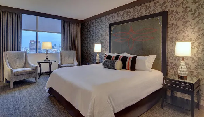 The image shows a well-appointed hotel room with a large bed elegant furniture and a city view through the window