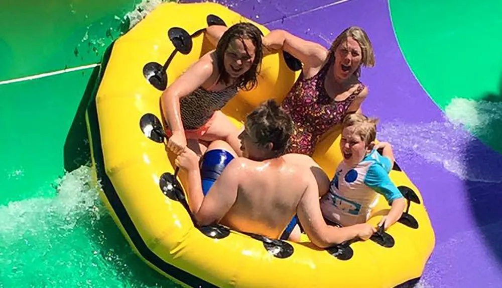 A group of people appear thrilled while riding together on a large yellow raft down a colorful water slide