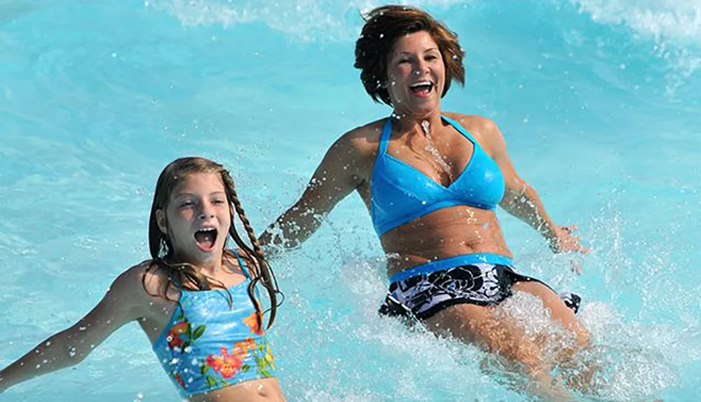 Two people an adult and a child appear joyful while splashing in a swimming pool