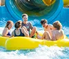 A group of friends is laughing and enjoying a sunlit ride down a water slide in a yellow raft