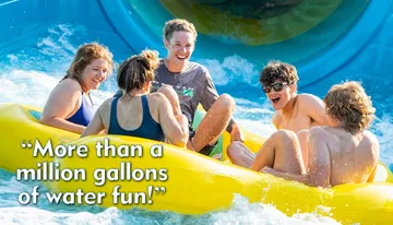 A group of friends is laughing and enjoying a sunlit ride down a water slide in a yellow raft.