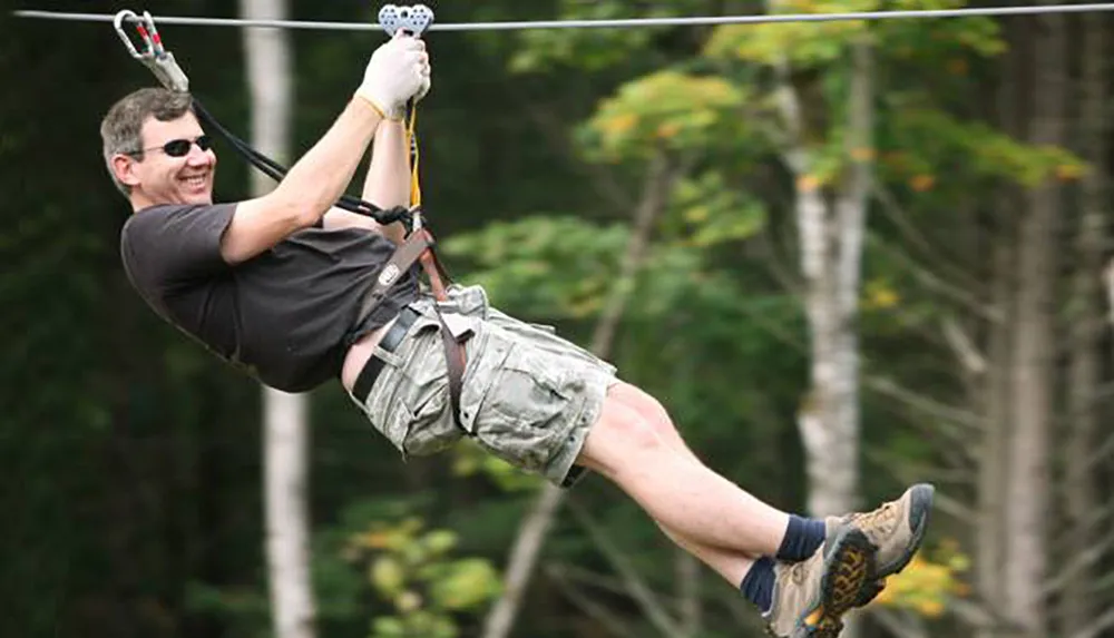 A smiling person is having fun ziplining through a wooded area