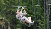 A person is gleefully zip-lining above a forested area.