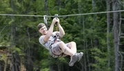 A person is gleefully zip-lining above a forested area.