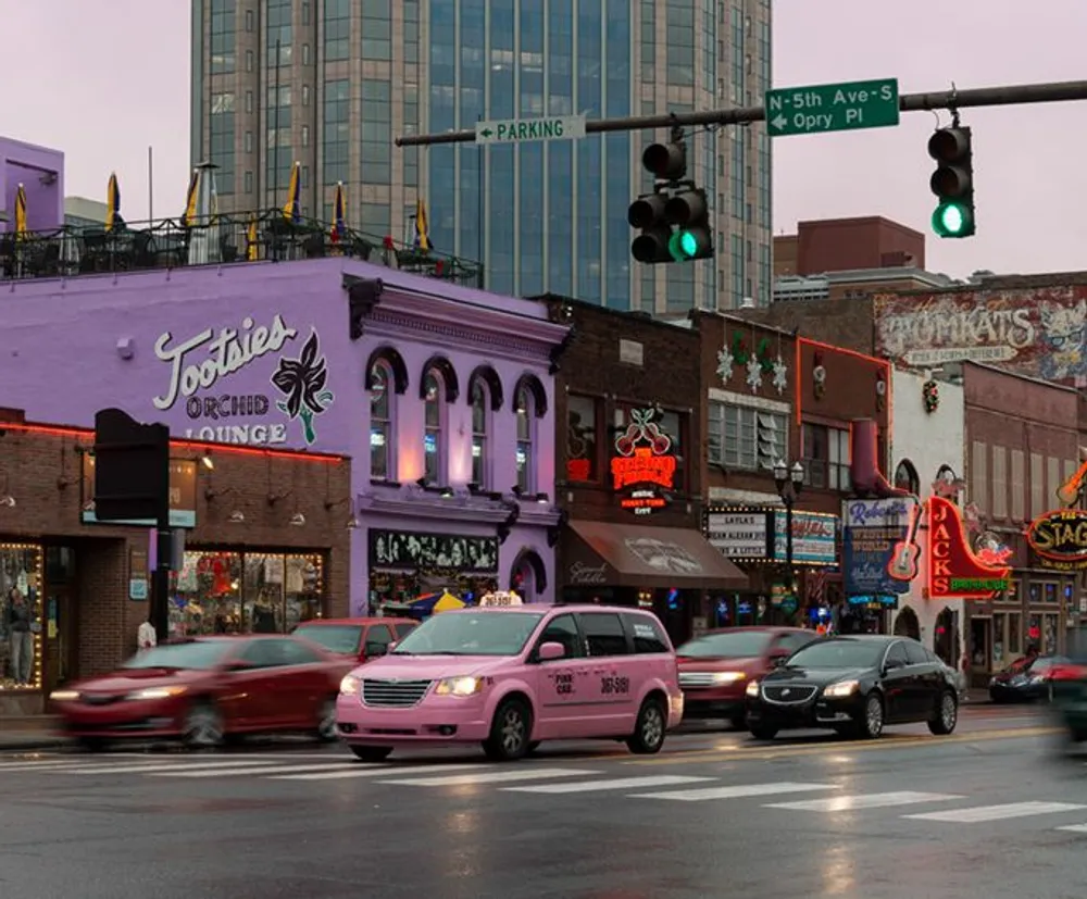 This image captures a bustling urban street scene at dusk with colorful neon signs including the iconic Tootsies Orchid Lounge against a backdrop of modern and traditional architecture