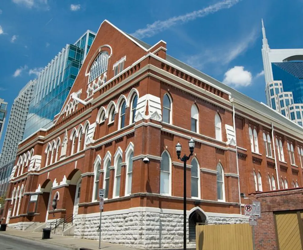The image shows a stately red brick building with arched windows juxtaposed against modern skyscrapers in the background under a clear blue sky