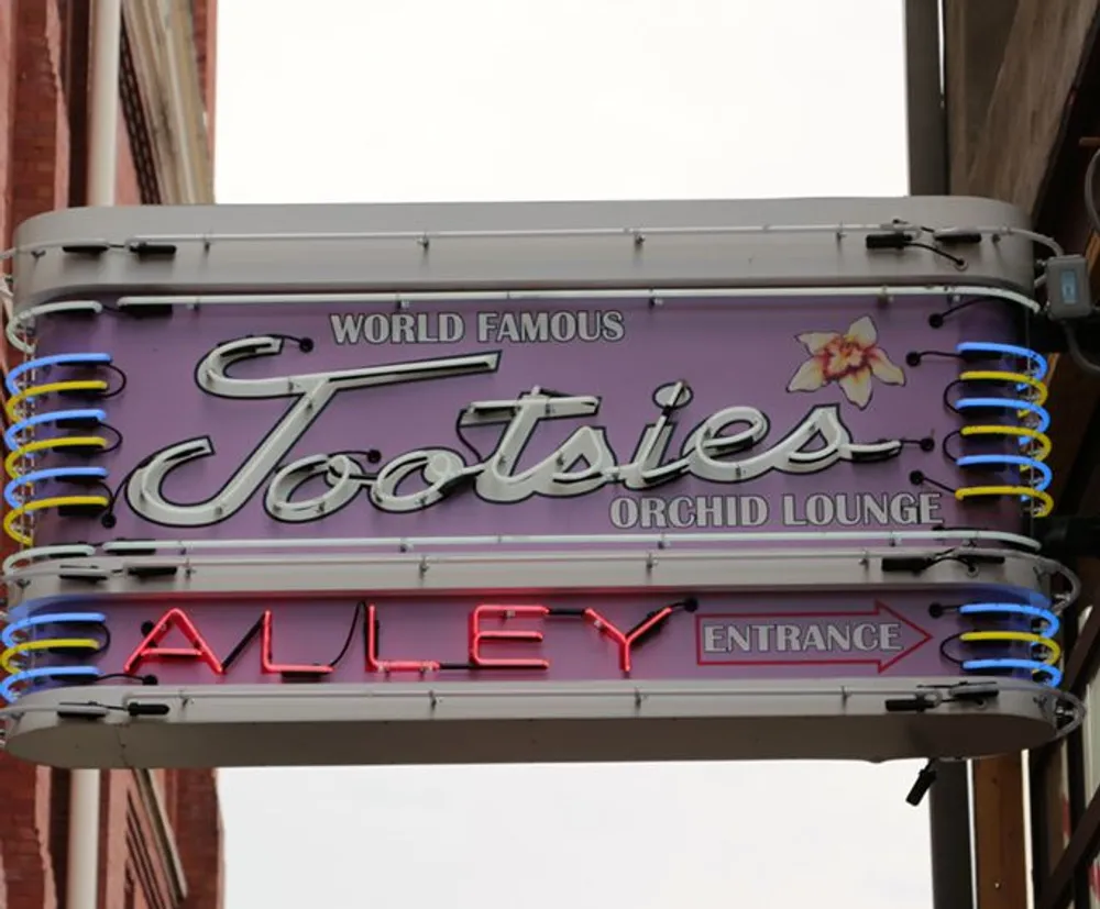 A vibrant neon sign reads World Famous Tootsies Orchid Lounge with directional arrows pointing towards an alley entrance