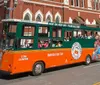 A green and orange trolley bus labeled Old Town Trolley Tours is carrying passengers on a hop-on hop-off tour in a city street