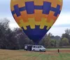 A colorful hot air balloon floats above a scenic landscape with fields trees and rolling hills under a partly cloudy sky