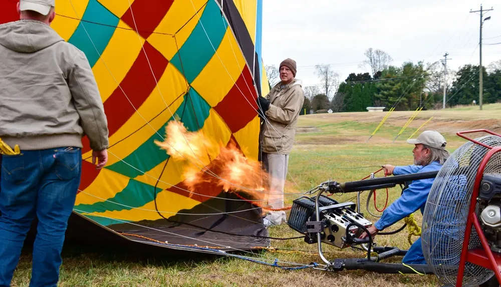 People are inflating a colorful hot air balloon on the ground using a burner that emits flames