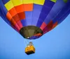A colorful hot air balloon with a yellow basket is floating against a clear blue sky