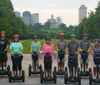 Two individuals are smiling for the camera while riding Segways on a path with the Nashville skyline in the background