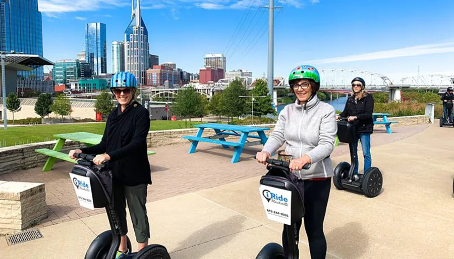 Two individuals are smiling for the camera while riding Segways on a path with the Nashville skyline in the background.