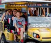 A group of people is enjoying a tour on a unique golf cart-like vehicle labeled JOYRIDE on a vibrant city street